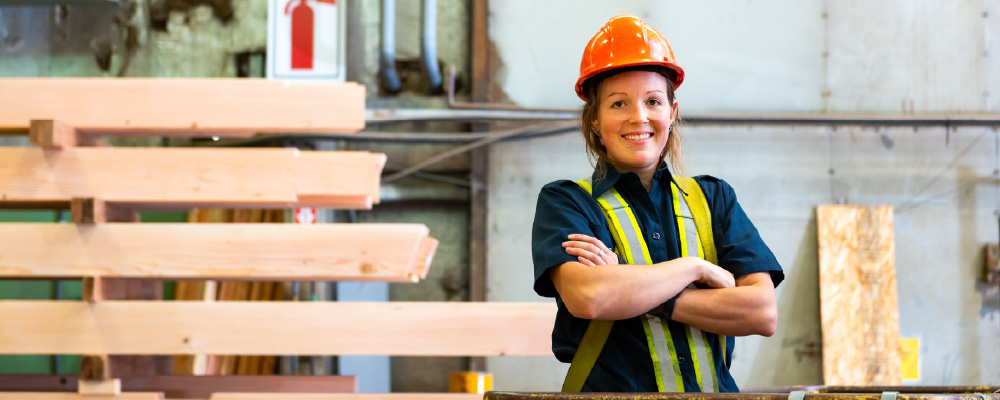 A woman worker in a hardhat stands smiling on a construction site.