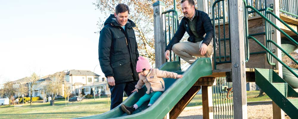 Premier David Eby and a young dad help a girl on a playground slide