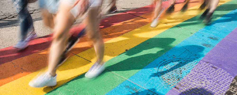 People walking across a rainbow crosswalk on a sunny day