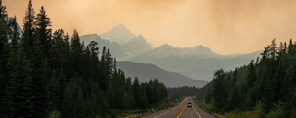 Heavy brown smoke in the air over a BC highway with one lone car driving in the distance