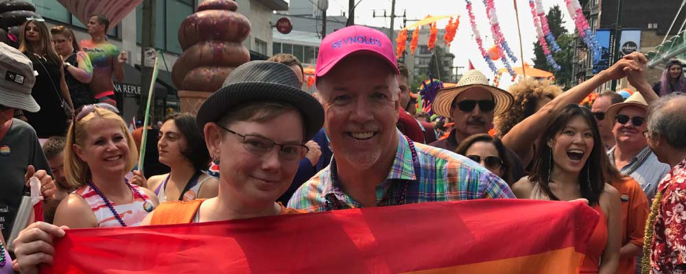 John Horgan and Adrienne Smith hold a pride flag and pose for a photo