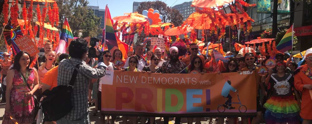 BC NDP and federal NDP supporters including Jagmeet Singh pose behind a giant NDP banner