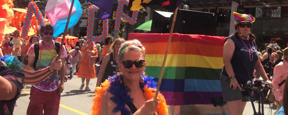 A pride parade marcher in front of a rainbow flag smiles for the camera