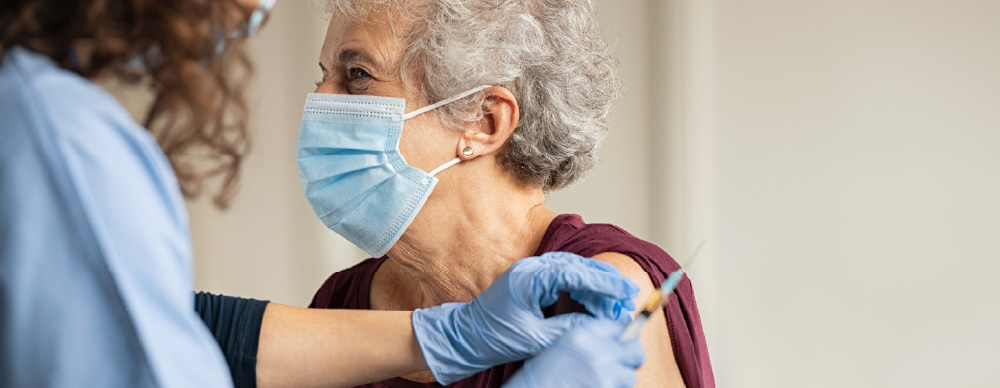 An older woman receives a vaccine booster in her upper arm from a health professional