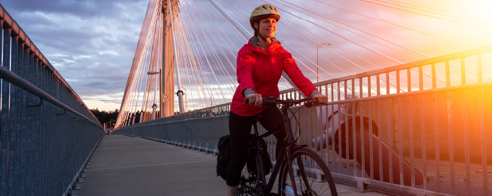 A woman rides her bike across the Port Mann bridge at sunset