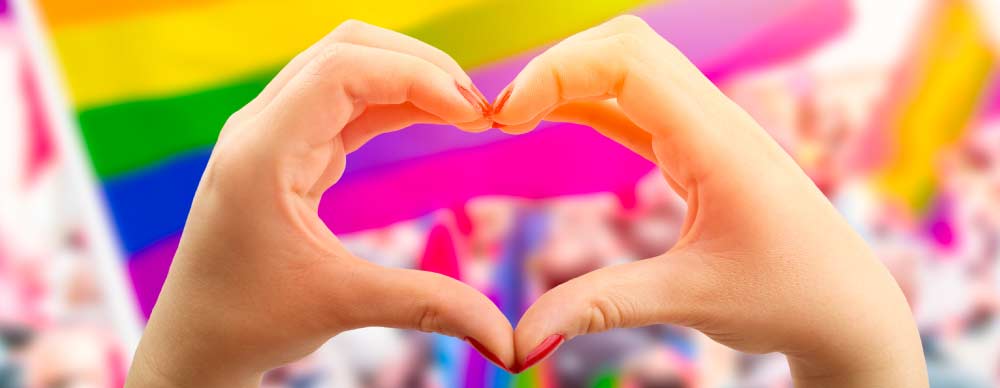 A kid makes a heart with their hands in front of a pride flag